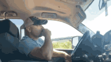 a man is sitting in the driver 's seat of a car drinking a beer .