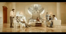 a group of people are gathered in a living room with a staircase in the background