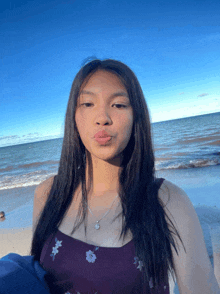 a woman in a purple dress stands on a beach with the ocean in the background