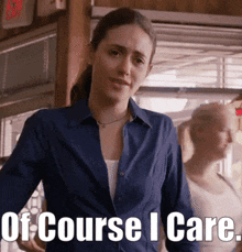 a woman in a blue shirt stands in front of a sign that says " of course i care "