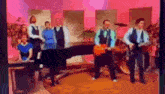 a group of people are standing around a piano and playing guitars .