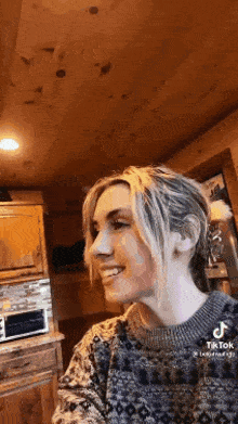 a woman wearing a sweater is smiling in a kitchen .
