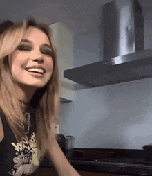a young woman is smiling in a kitchen with a stainless steel exhaust fan .