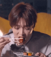 a young man is eating food with chopsticks .