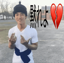 a man wearing a white shirt and a black beanie stands in front of a broken heart with chinese writing behind him