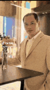 a man in a suit is standing next to a table with flowers in a vase .