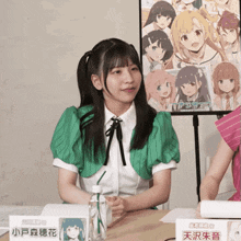 a girl in a green shirt sits at a table in front of a sign that says ' a ' on it