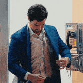 a man in a blue suit is standing next to a pay phone