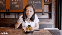 a woman is sitting at a table with a plate of food and a chalkboard that says $ 7 cocktails