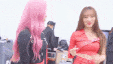 two women with pink hair are standing next to each other and talking .