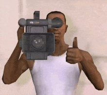 a man in a white tank top is holding a camera and giving a thumbs up .