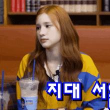 a girl in a yellow and blue jacket is sitting at a table with a cup of water with a blue straw