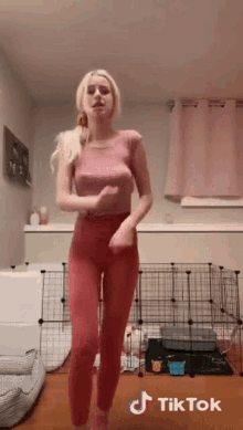 a woman in a pink top and red pants is dancing in front of a dog cage and a dog bed ..
