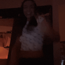 a woman in a white shirt stands in the dark