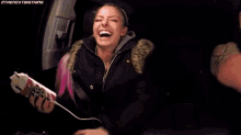 a woman in a black jacket is smiling while sitting in a car .