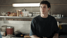 a young man in a black shirt stands in front of a kitchen counter