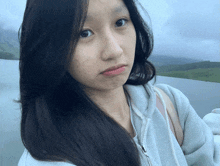 a woman with long black hair is wearing a gray hoodie