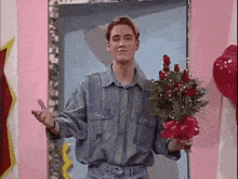 a man in a denim shirt is holding a bouquet of roses in front of a pink wall .