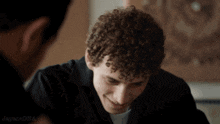 a man with curly hair is smiling and laughing while another man looks on ..