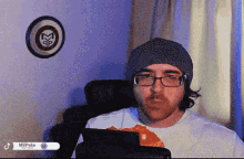 a man wearing a beanie and glasses is sitting in front of a mvpete sign