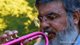 a man with a beard wearing glasses is playing a pink trumpet