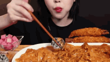 a woman is eating a plate of food with chopsticks and a bowl of pickles .