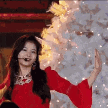 a woman in a red dress is dancing in front of a christmas tree