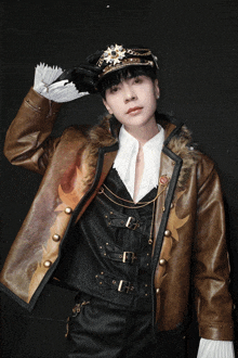 a man wearing a hat and a leather jacket stands in front of a black background