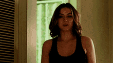 a woman in a black tank top is standing next to a window