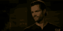 a man with a beard is smiling while talking to another man in a dark room .
