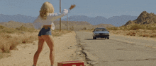 a woman stands on a suitcase on the side of a road
