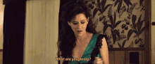 a woman in a green dress is sitting on a bed and asking what are you doing .
