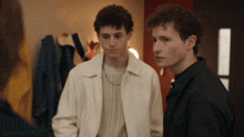 two young men are standing next to each other in a room with clothes hanging on a rack behind them