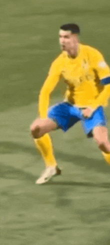 a soccer player in a yellow shirt and blue shorts is kicking a soccer ball on a field .