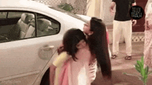a couple of women hugging each other in front of a car .