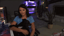 a woman in a blue shirt holds a black dog in her arms in front of a display case with the number 9 on it