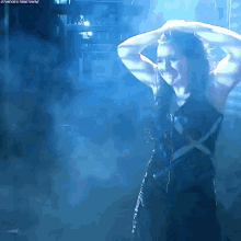 a woman in a black dress is standing in a dark room with blue smoke coming out of the ceiling .