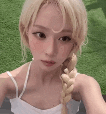 a girl with blonde hair is taking a selfie while wearing a white tank top .