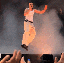 a man in a white tank top is jumping in the air with a microphone in his hand