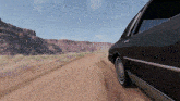 a car is driving down a dirt road in the desert .