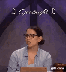 a woman wearing glasses is sitting at a table with a tablet in front of her and says goodnight .