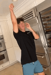 a man in a black shirt and blue shorts is standing in a kitchen
