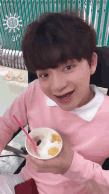a boy in a pink shirt is holding a cup of ice cream with a pink straw
