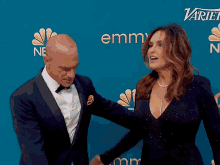 a man in a tuxedo and a woman in a black dress are holding hands in front of a variety logo