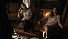 two women are sitting in front of a fireplace in a living room