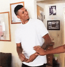 a man in a white t-shirt is being slapped by another man in a living room