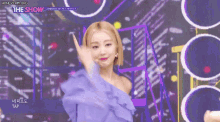 a woman in a purple dress is giving a peace sign while standing on a stage .
