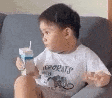 a young boy is sitting on a couch drinking milk from a carton .