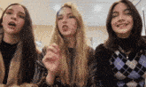 three young women are standing next to each other in a room and talking .
