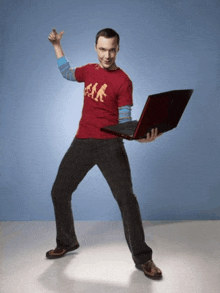 a man wearing a red shirt that says ' a.k. ' on it is holding a laptop